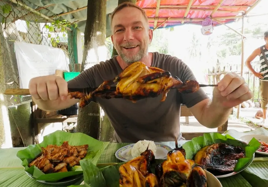 Geoff enjoying native chicken inasal at Chay Letty’s in Bacolod, holding a perfectly grilled whole chicken on a skewer. One of Bacolod's 20 must-try dishes