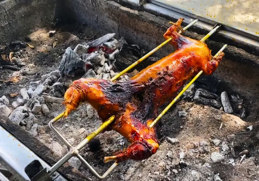 Lechon-style rabbit roasting whole over charcoal on a manual rotisserie.