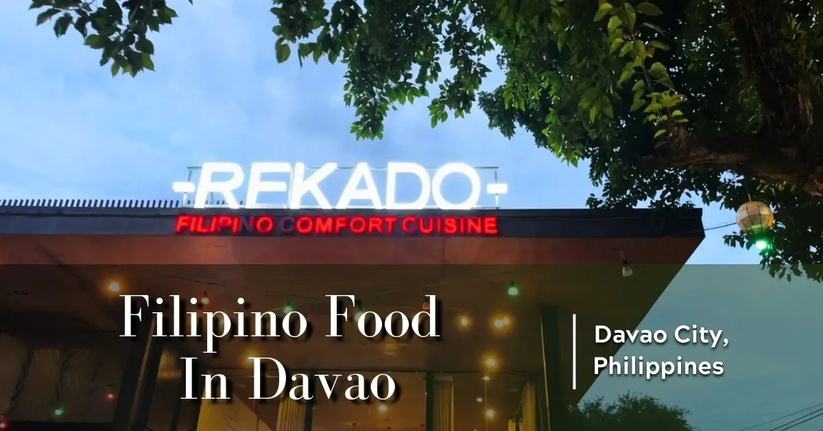 Front signage of Rekado Filipino Comfort Cuisine in Davao at dusk, with glowing lights and tree canopy overhead