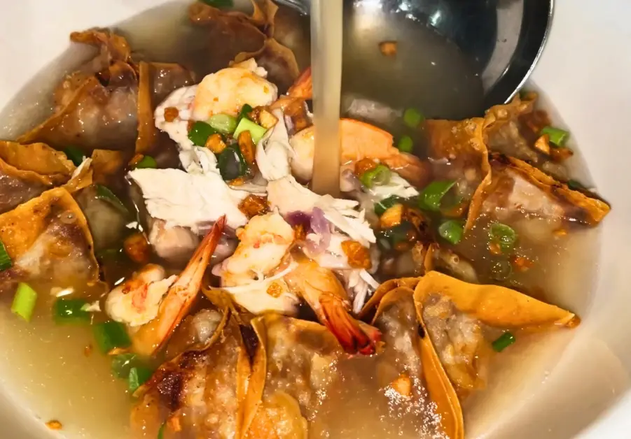 Hot pork and chicken broth being poured over dumplings, shrimp, and chicken at Rekado in Davao