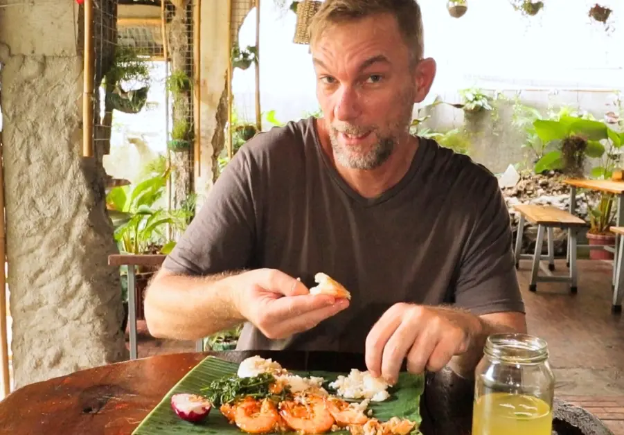 Geoff eating shrimp and rice with his hands at Gubat QC, seated at the table with calamansi juice