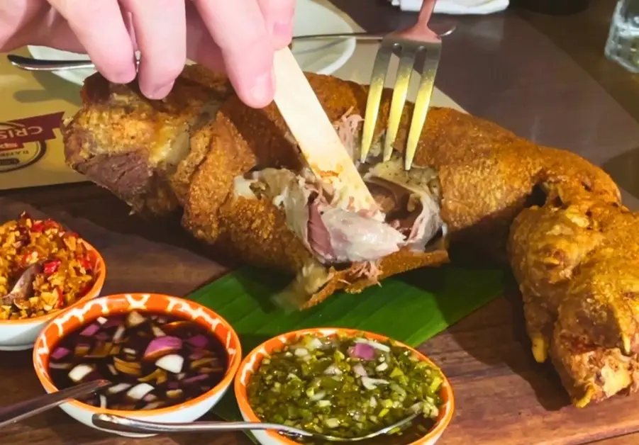 Where to Eat in Quezon City: 11 Must-Try Locations Crispy pata being torn with a popsicle stick at Livestock Restaurant Bar in QC.