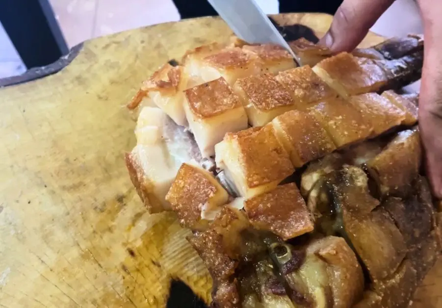 Knife slicing through crispy fried Kapalmuks pork face on chopping board