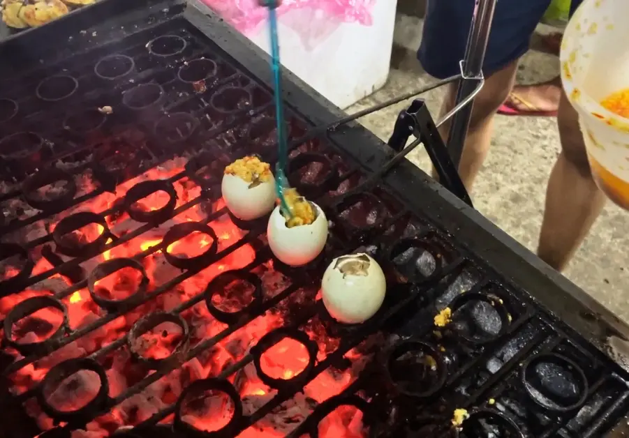 Balut eggs grilling in custom grate slots, stuffed with garlic and vinegar.