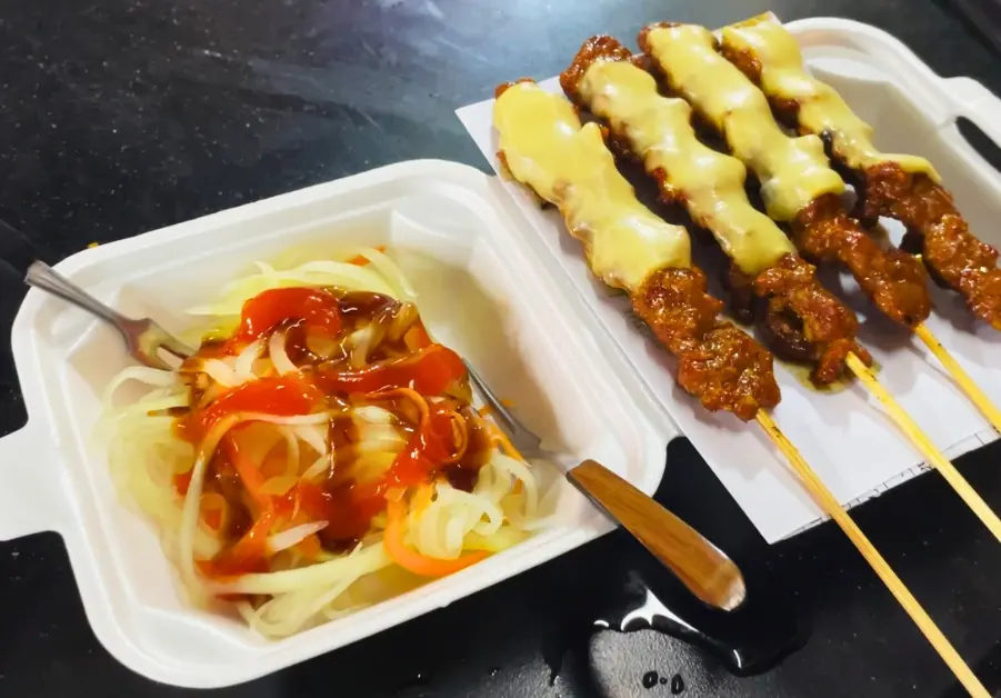 Cheese-covered Cambodian beef skewers with pickled papaya salad, one of the street food staples at Hồ Thị Kỷ Night Market in Saigon.