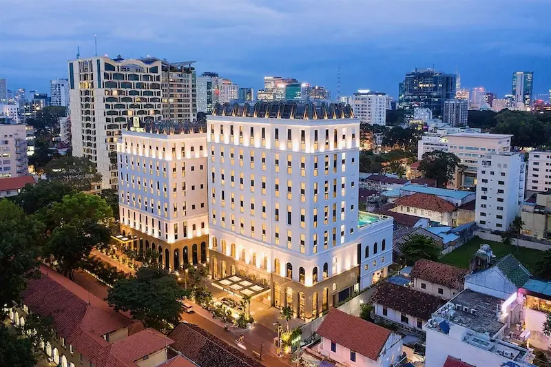 Colonial-style exterior of Mai House Saigon lit up at night in District 3 with skyline views in the background