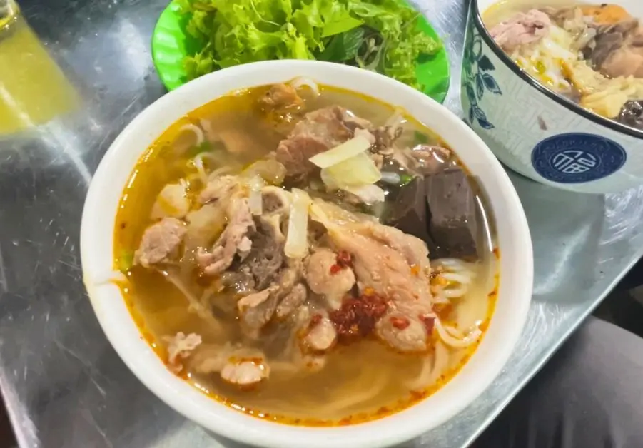 Bowl of spicy bún bò Huế noodle soup with beef and herbs