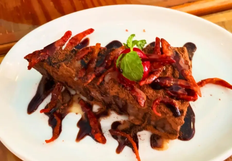 Goto Believe: Kapitolyo's Mind-Blowing Congee Champorado cheesecake slice topped with cocoa, dried fish, and chocolate drizzle