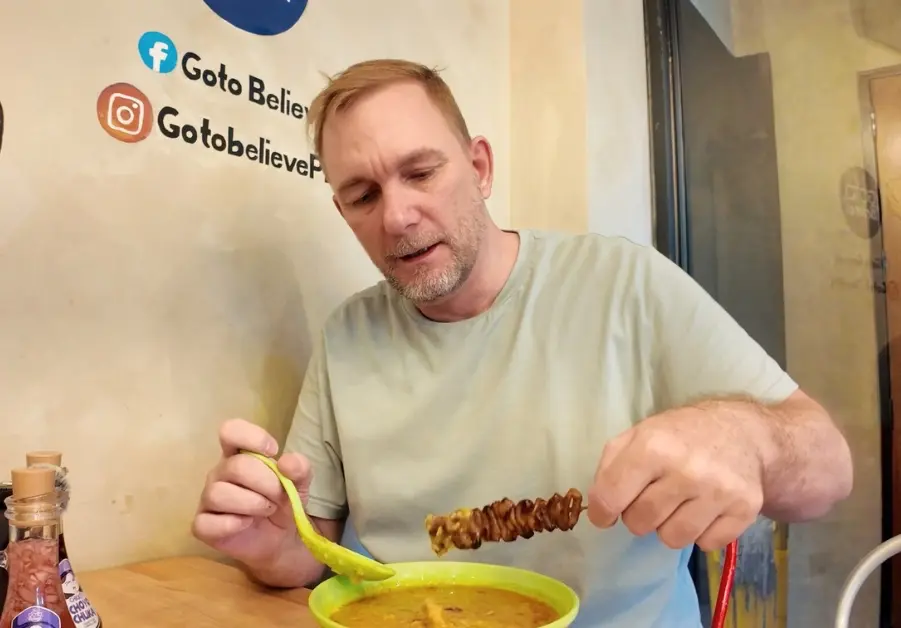 Goto Believe: Kapitolyo's Mind-Blowing Congee Geoff eating goto with isaw skewer inside Goto Believe Kapitolyo branch