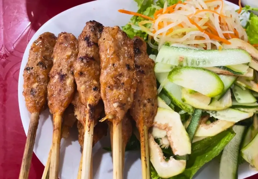 Plate of grilled nem lụi pork skewers with vegetables in Hue