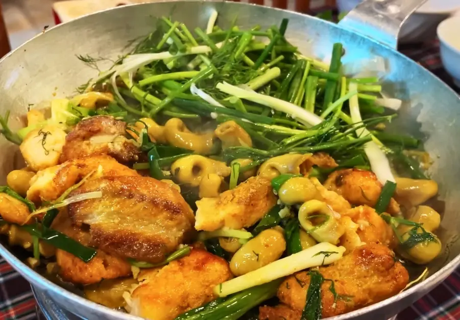 Close-up of turmeric-spiced catfish and dill cooking on a hotplate at Anh Vũ Hanoi.