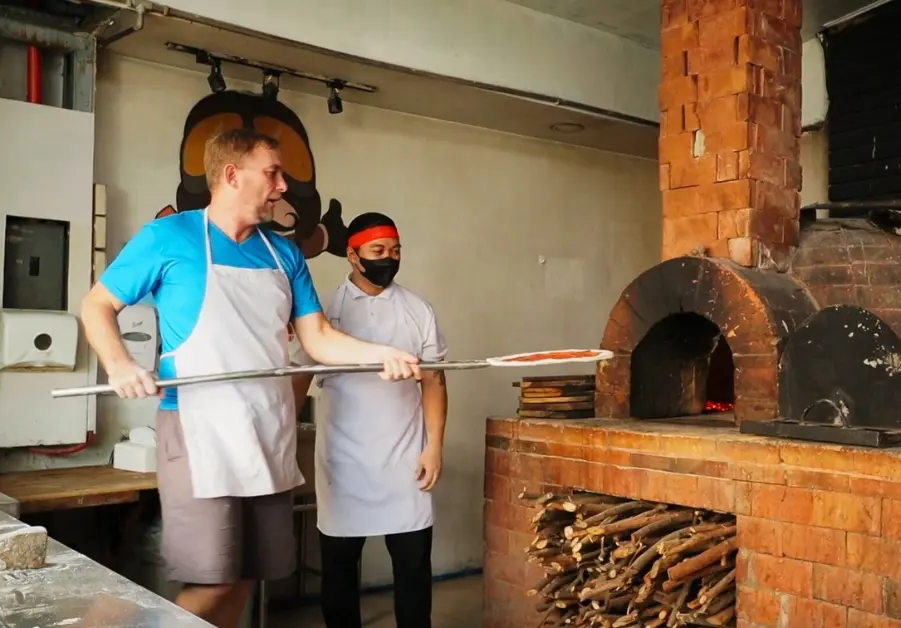 geoff making pizza with chef beside the brick oven at amare la cucina