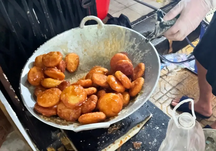 Freshly fried bánh rán coated in syrup inside a wok at a Hanoi street kitchen