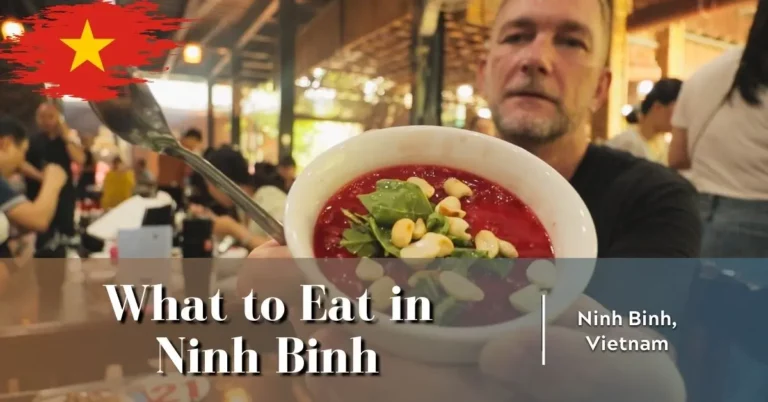 Geoff offering a small white bowl of raw, crimson Tiết Canh (duck blood pudding) topped with crunchy peanuts and herbs, daring the reader to try it.